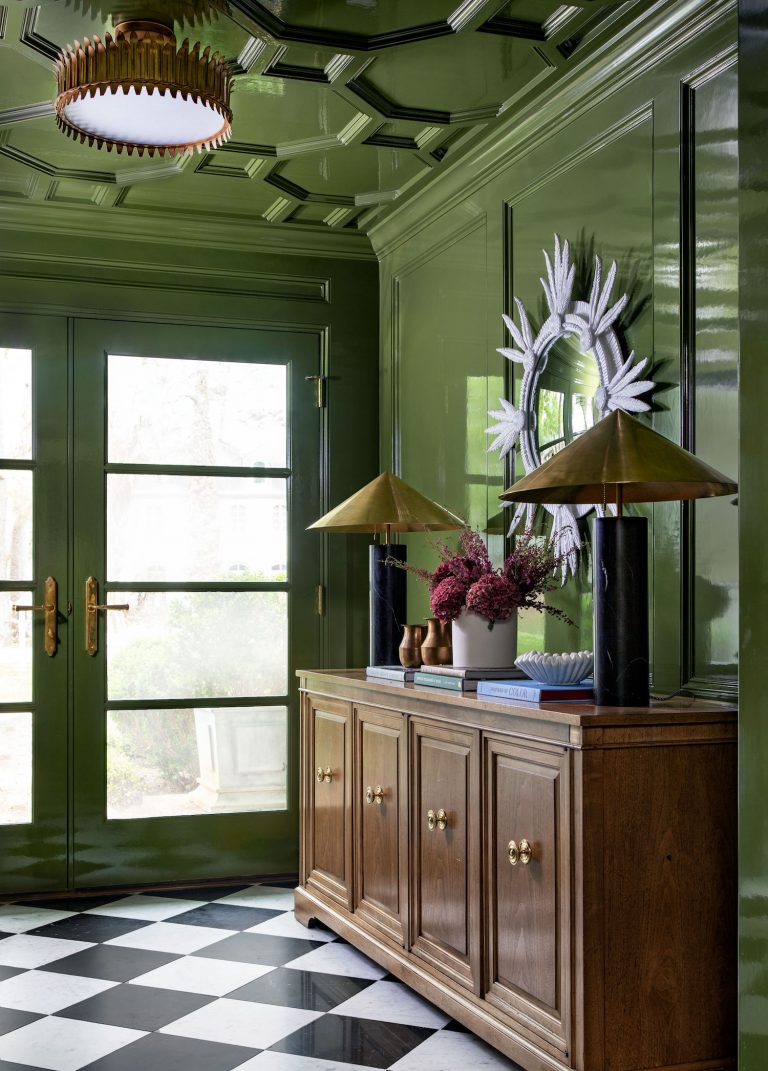 Deep green room with french doors, black and white checkered floor and wooden buffet chest.