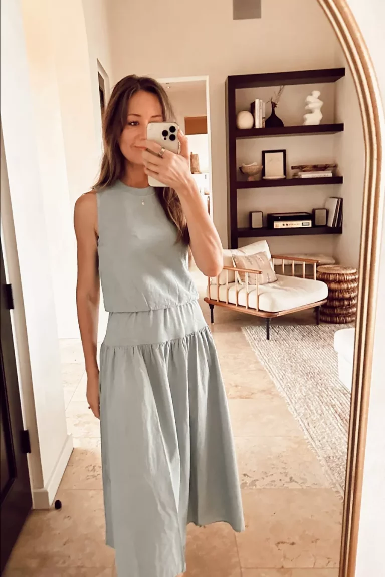 A woman in a light blue dress taking a selfie in the mirror