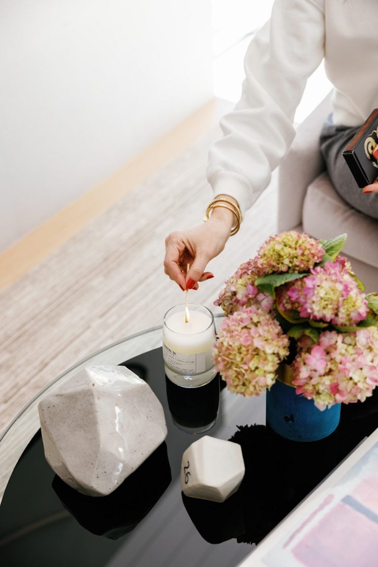 Woman with pink hydrangeas and red nails lighting a white candle on a black table. 