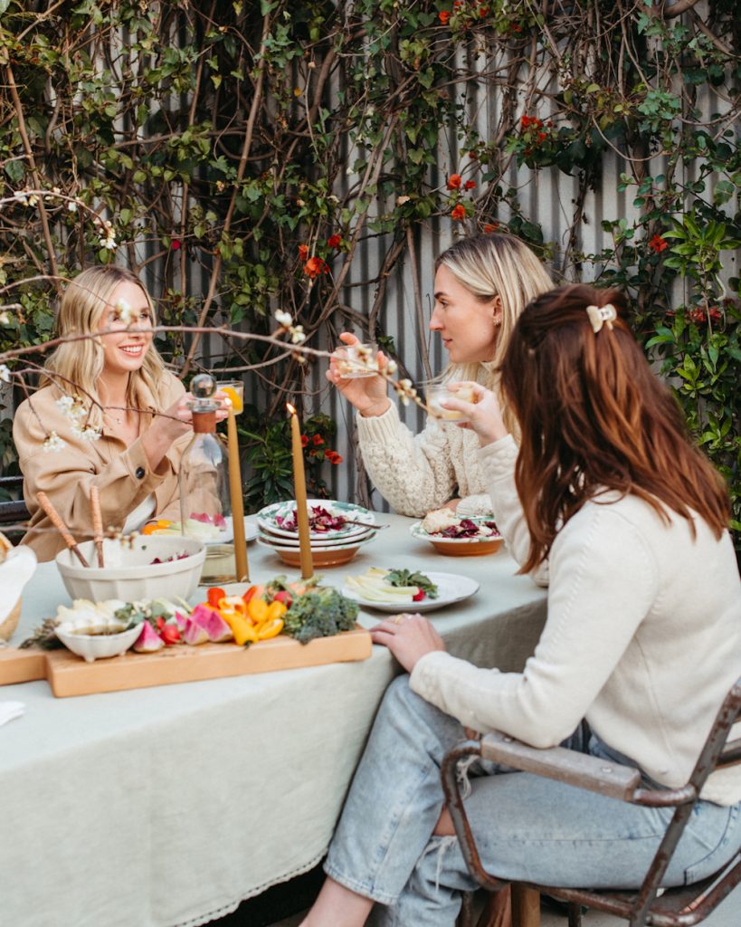 Three women talking around outdoor dinner table.