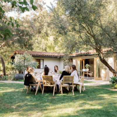 Women sitting around outdoor dining table in the middle of green grass yard.