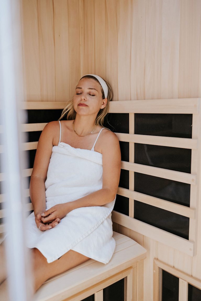 Blonde woman wrapped in towel laying in sauna.
