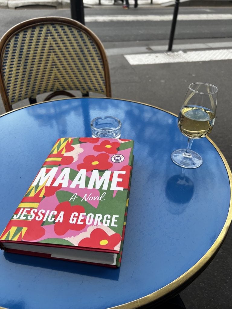 Maame book and a glass of white wine on a blue table at La Fontaine de Belleville in Paris.