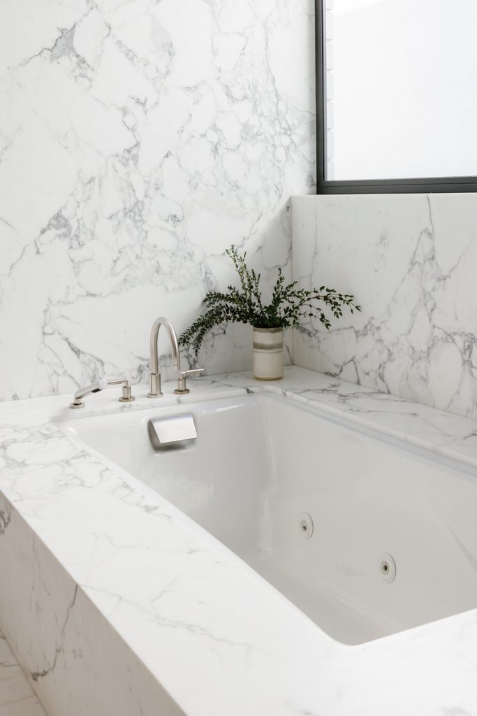 Minimalist marble bathtub with eucalyptus in vase.