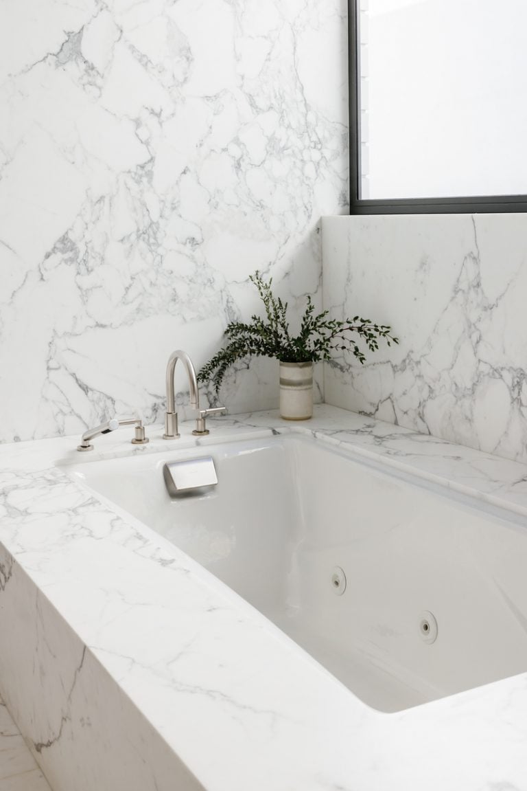 A simple marble bathtub with eucalyptus in a vase.