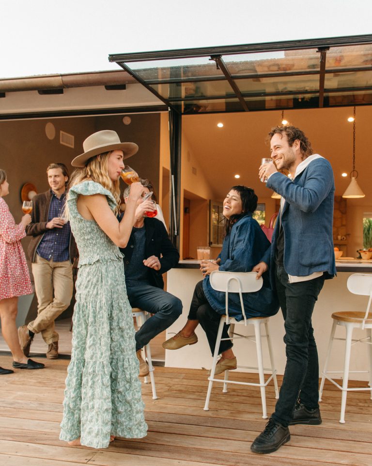 Group of people drinking and talking outdoors on the deck of their home.