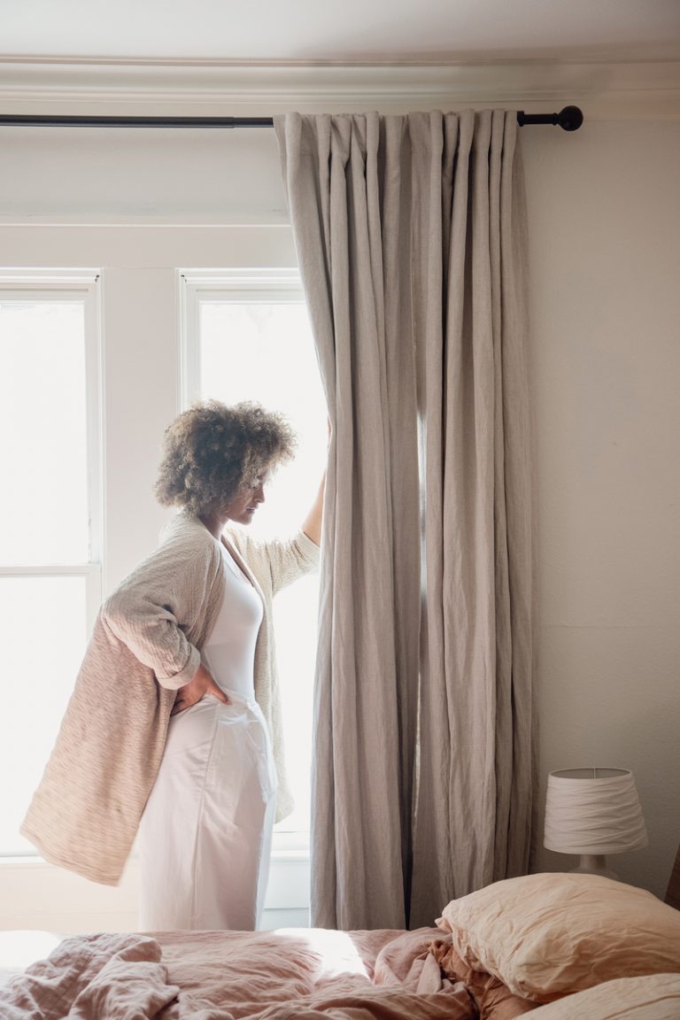 woman pushing back curtains, acupuncture mat