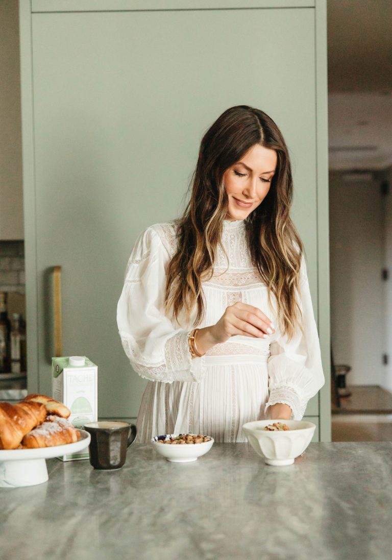 Mujer con cabello castaño largo preparando avena en un tazón blanco en la cocina.