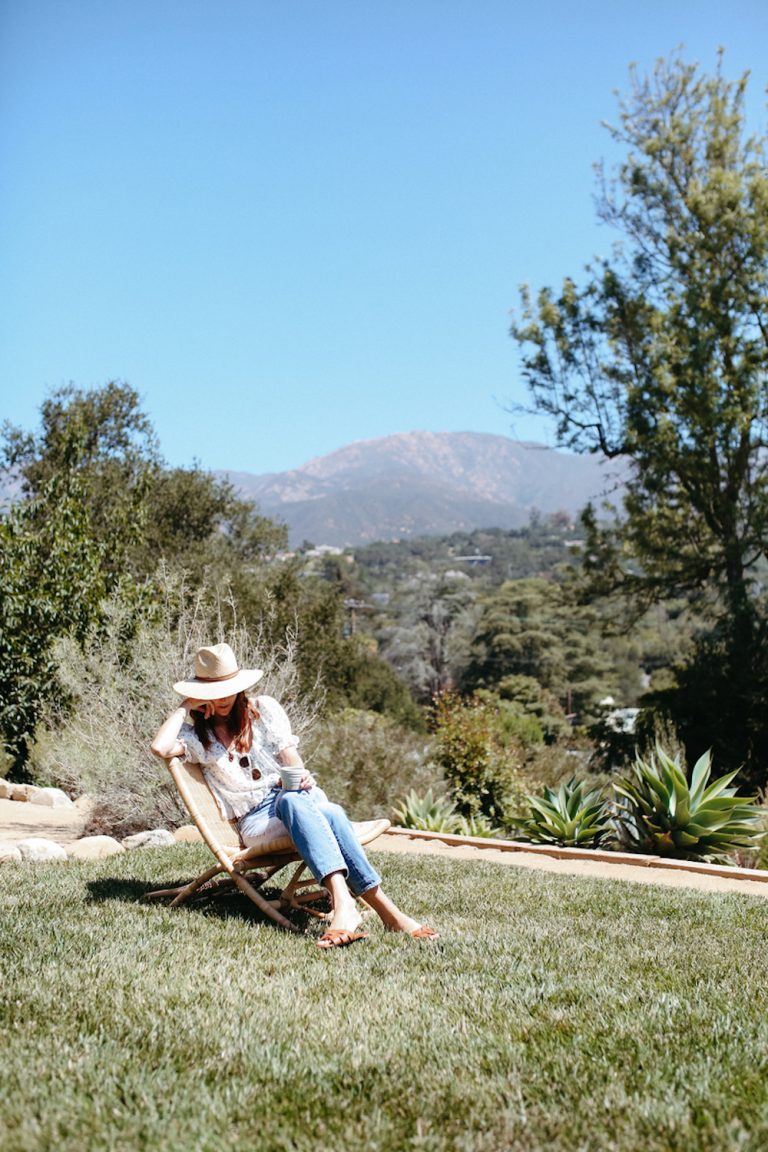 Red-head woman wearing jeans and sunhat sitting in lawn chair on grass.