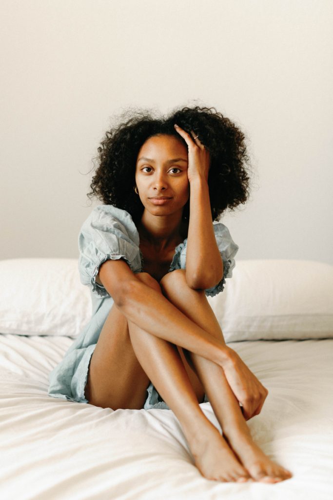 Black woman sitting on bed in blue nightgown.