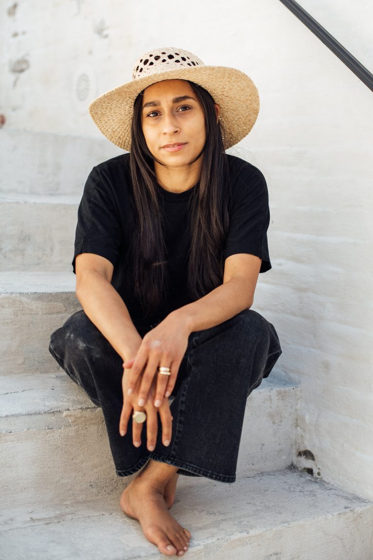 Brunette woman wearing sun hat, black shirt and black pants sitting on stone steps.