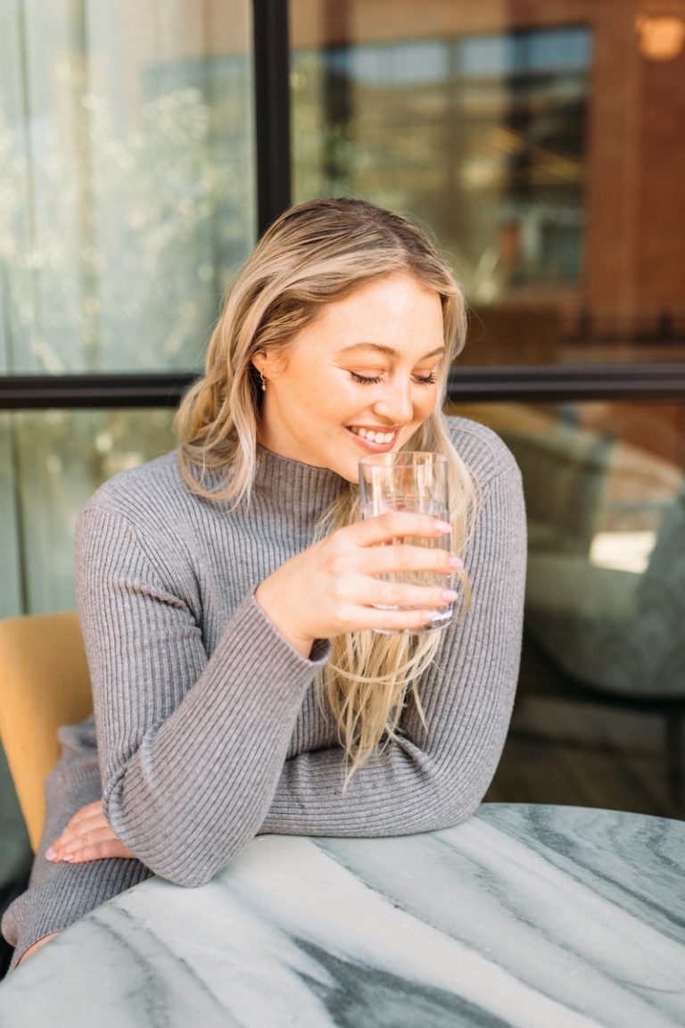 Blonde woman drinking water at marble table.