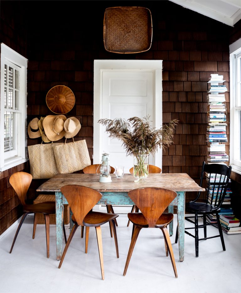 Porch dining table with mismatched vintage chairs and clear vase.