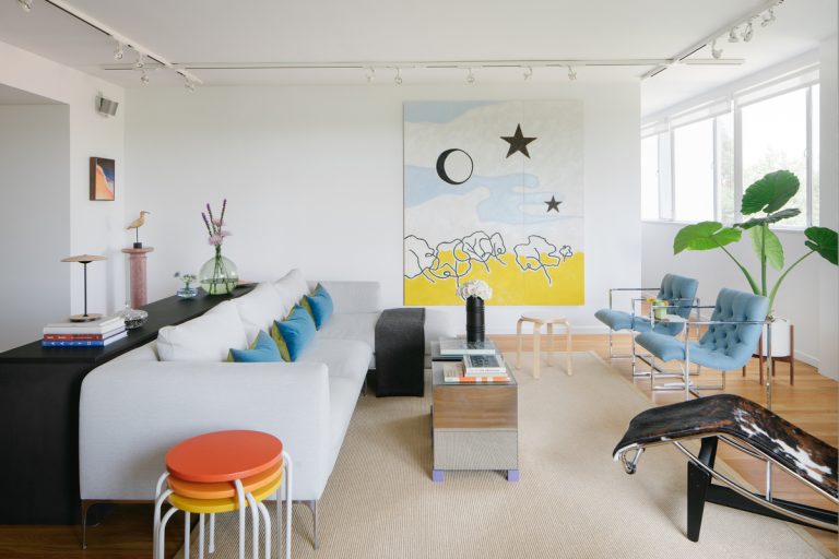 Sala de estar blanca y moderna con arte abstracto, sofá blanco y alfombra color crema.