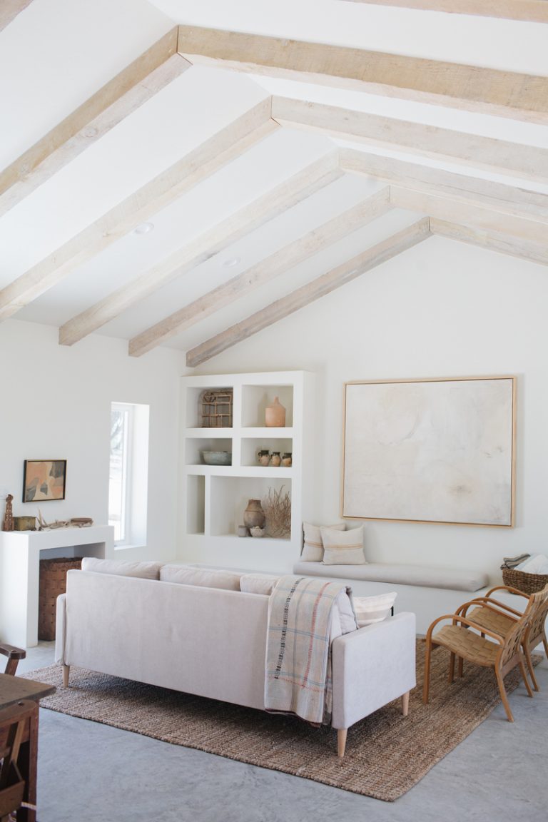Una sala de estar neutra y minimalista con paredes blancas, acentos naturales y vigas de madera clara.