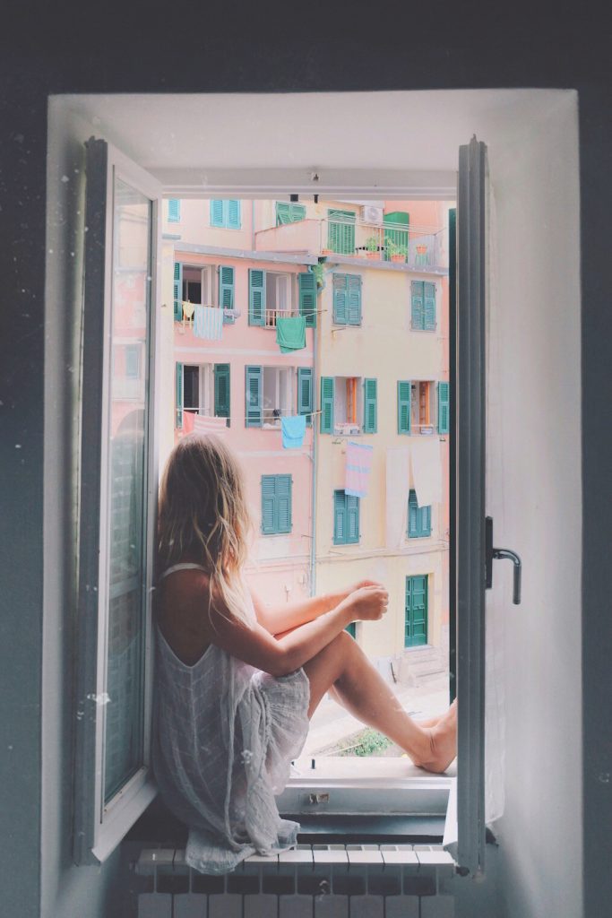 Blonde woman wearing white dress sitting in window in Cinque Terre.