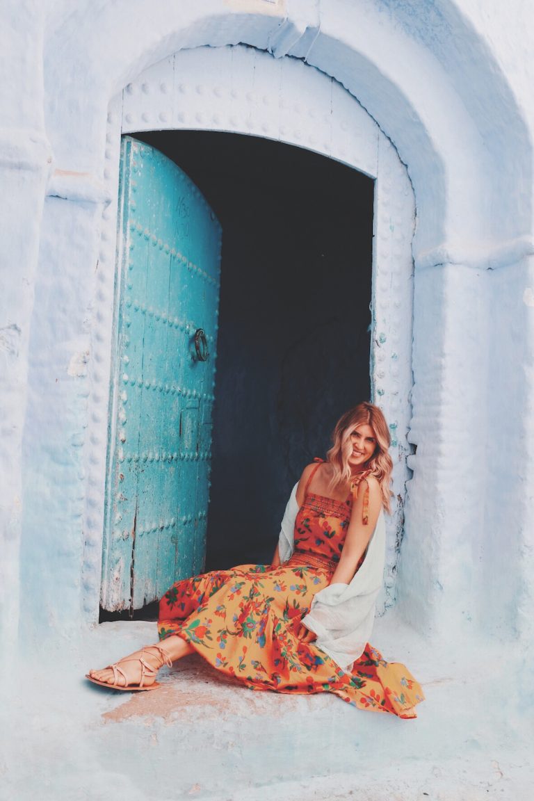 Anna Kloots sentada em uma escada de pedra azul clara no Marrocos. 