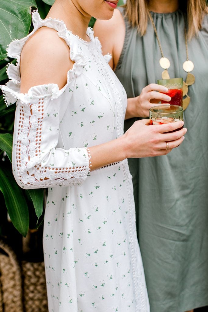 Woman in white long-sleeved floral dress holding cocktail.
