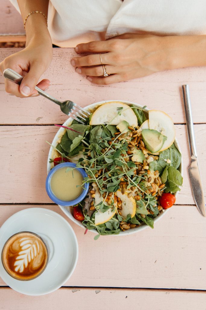 Plate of green salad next to latte on pink picnic table at Better Half Coffee in Austin, Texas.