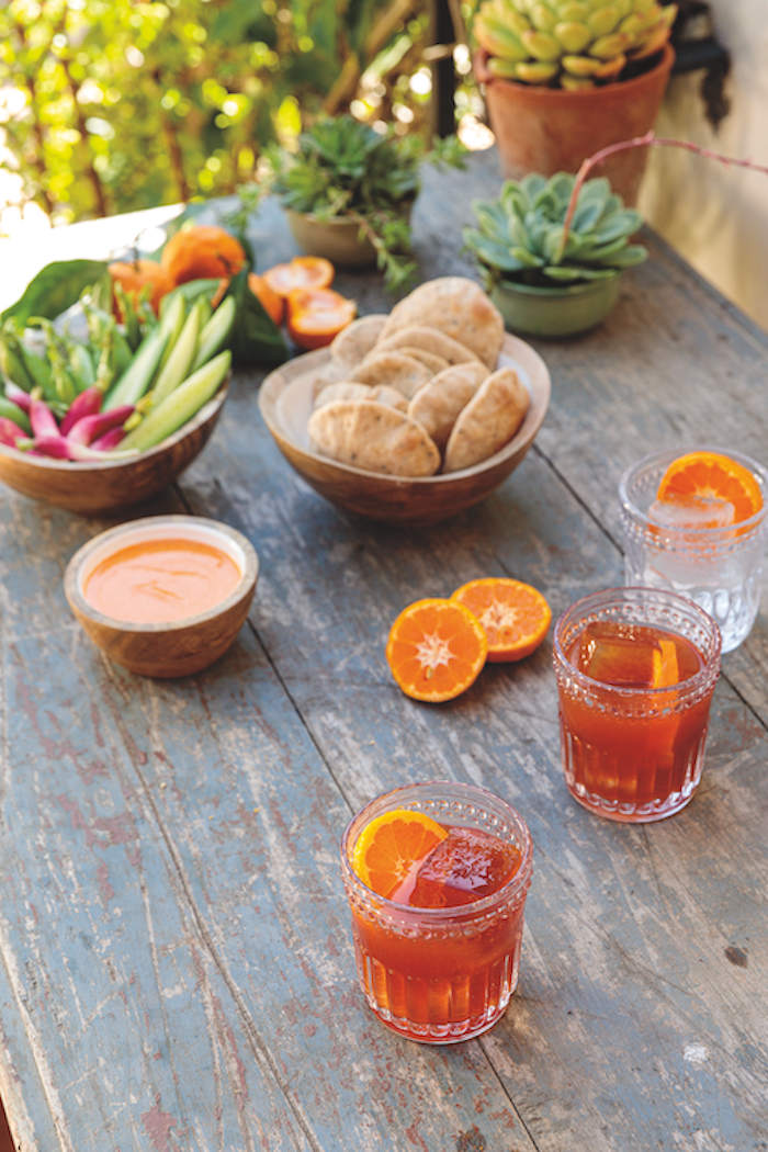 Three cocktail glasses and appetizers on wooden picnic table.