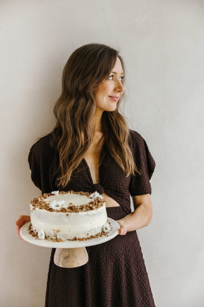 Camille Styles wearing brown short-sleeved dress holding carrot cake.