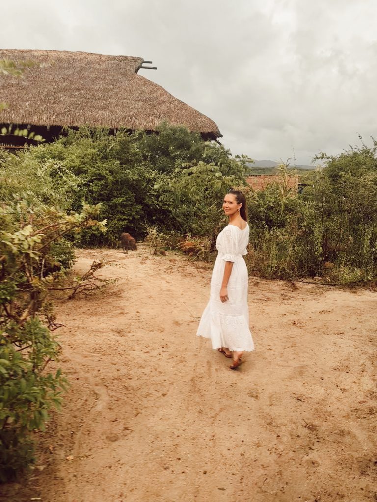 Camille Styles con un vestido largo blanco caminando sobre la arena en Puerto Escondido.
