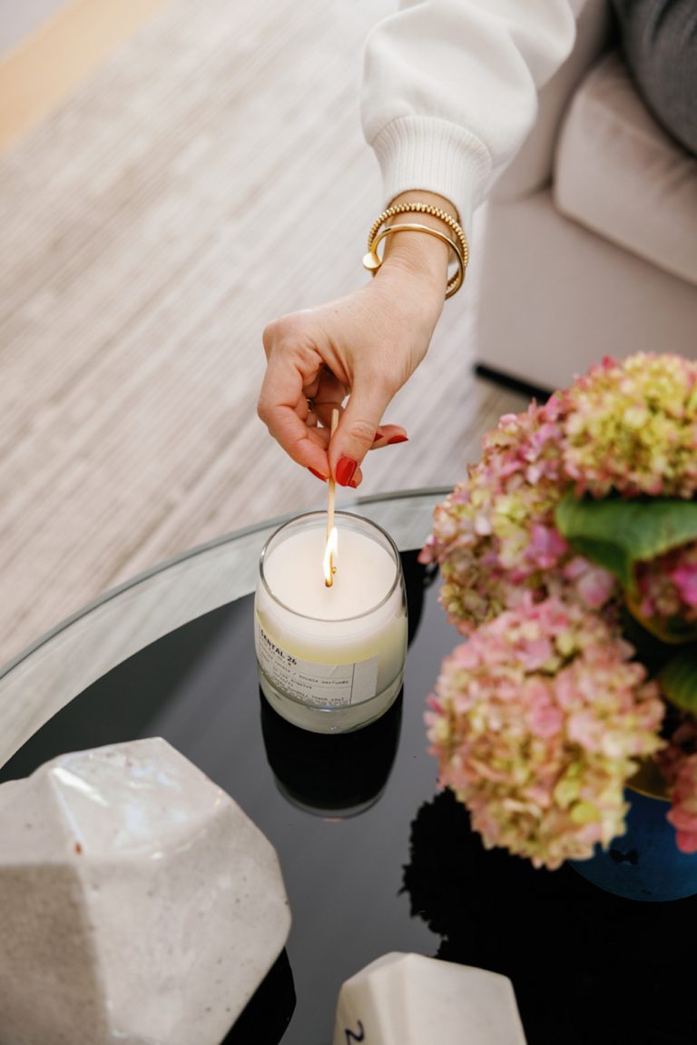 Woman wearing gold bangles with red manicure lighting candle on black coffee table with crystals and hydrangeas.
