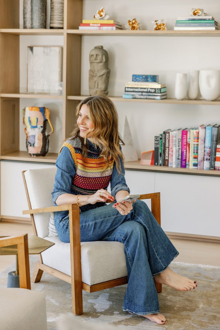 Brunette woman wearing sweater and jeans using cell phone sitting on armchair.
