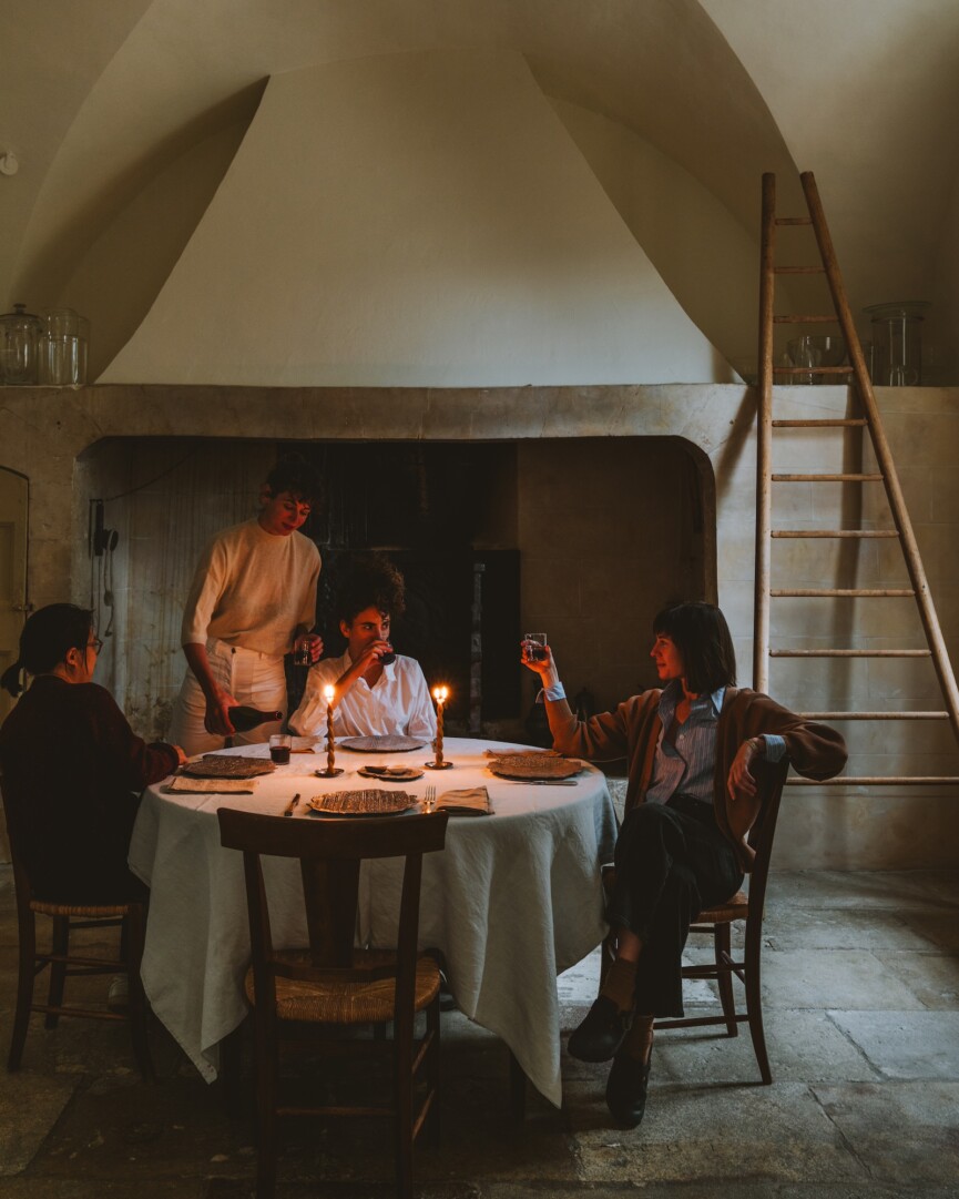 Guests gathered around a candlelit round table with a white tablecloth in a softly lit dining room.