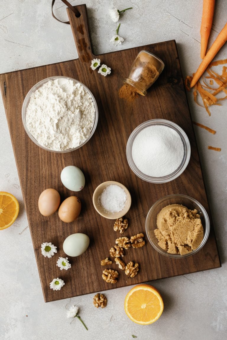 Eggs, flour, walnuts, brown sugar, and oranges on dark wood cutting board.