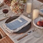 Celebration table with pink and green hydrangeas, candles in ribbed glass holders, and a blue menu on a linen napkin.