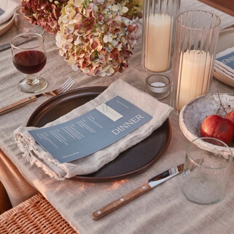 Celebration table with pink and green hydrangeas, candles in ribbed glass holders, and a blue menu on a linen napkin.