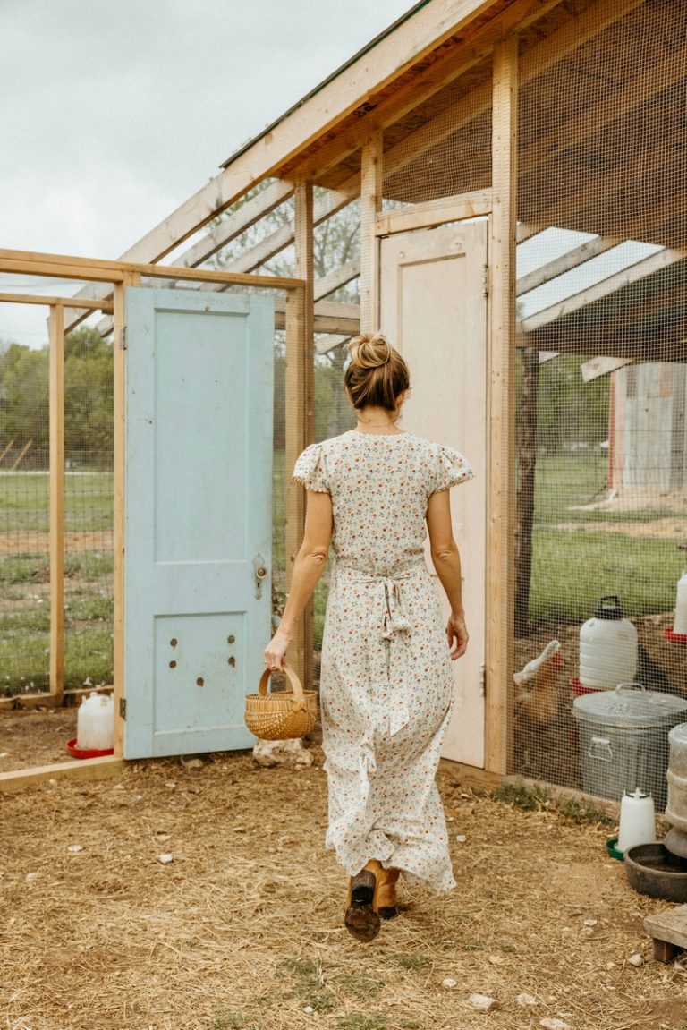 Woman wearing cottagecore aesthetic dress collecting eggs from chicken coop.