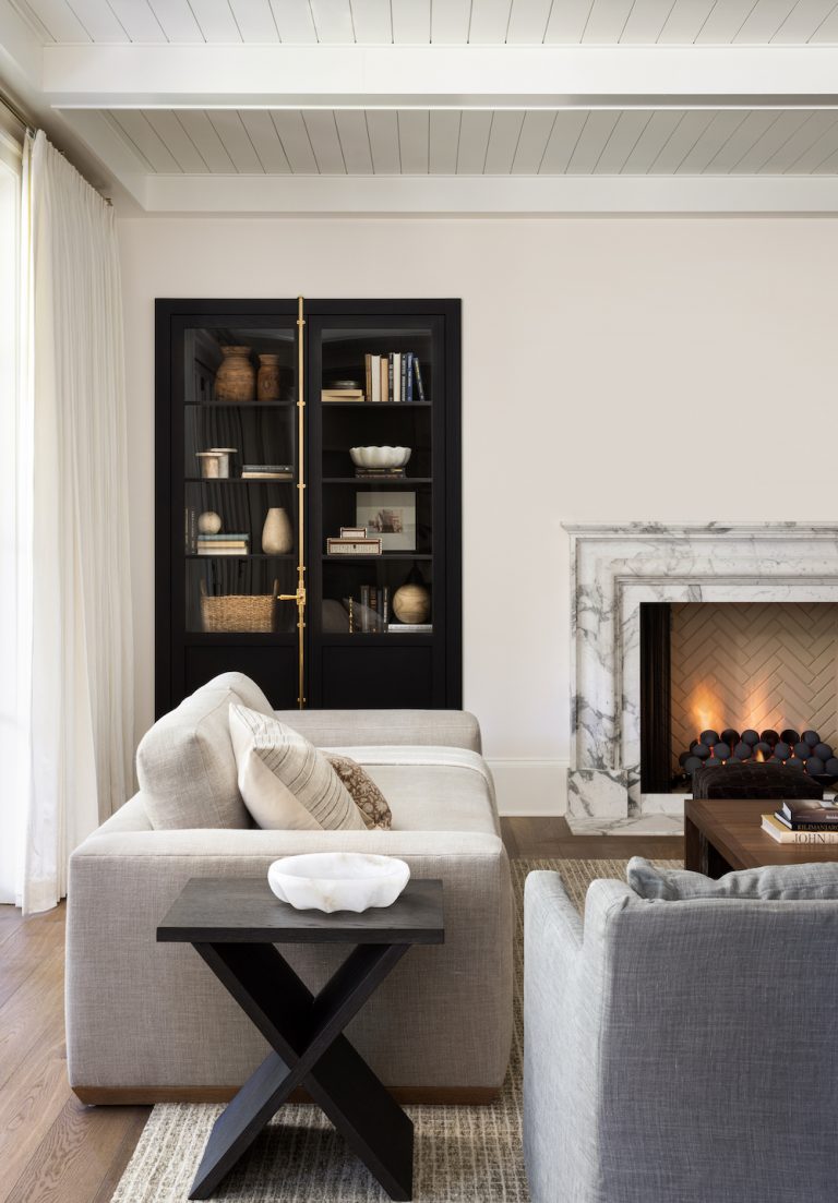 Tendência de luxo tranquila em aconchegante sala de estar branca com estante preta, lareira de mármore e dois sofás de cores neutras.