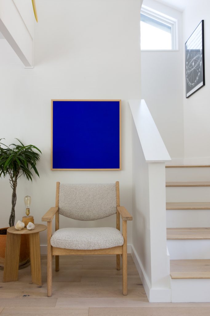 Modern and minimal stairway with white walls, Yves Klein blue painting, and simple armchair.