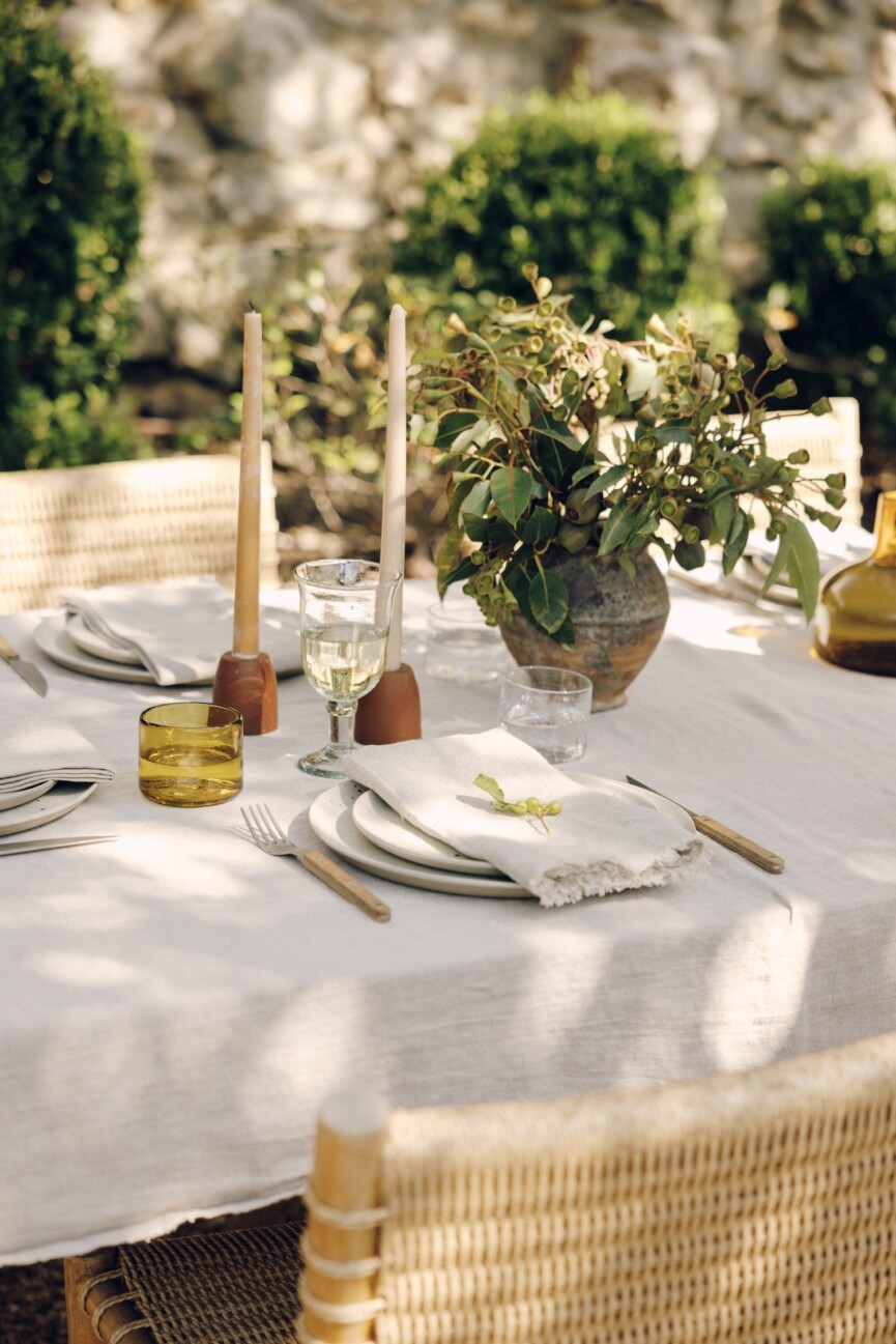 Outdoor table with white daffodils, a dark pitcher, linen napkins, and a leafy sprig at each place setting.