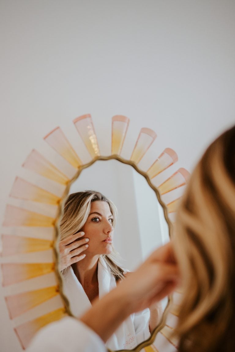 Blonde woman looking at face in mirror.