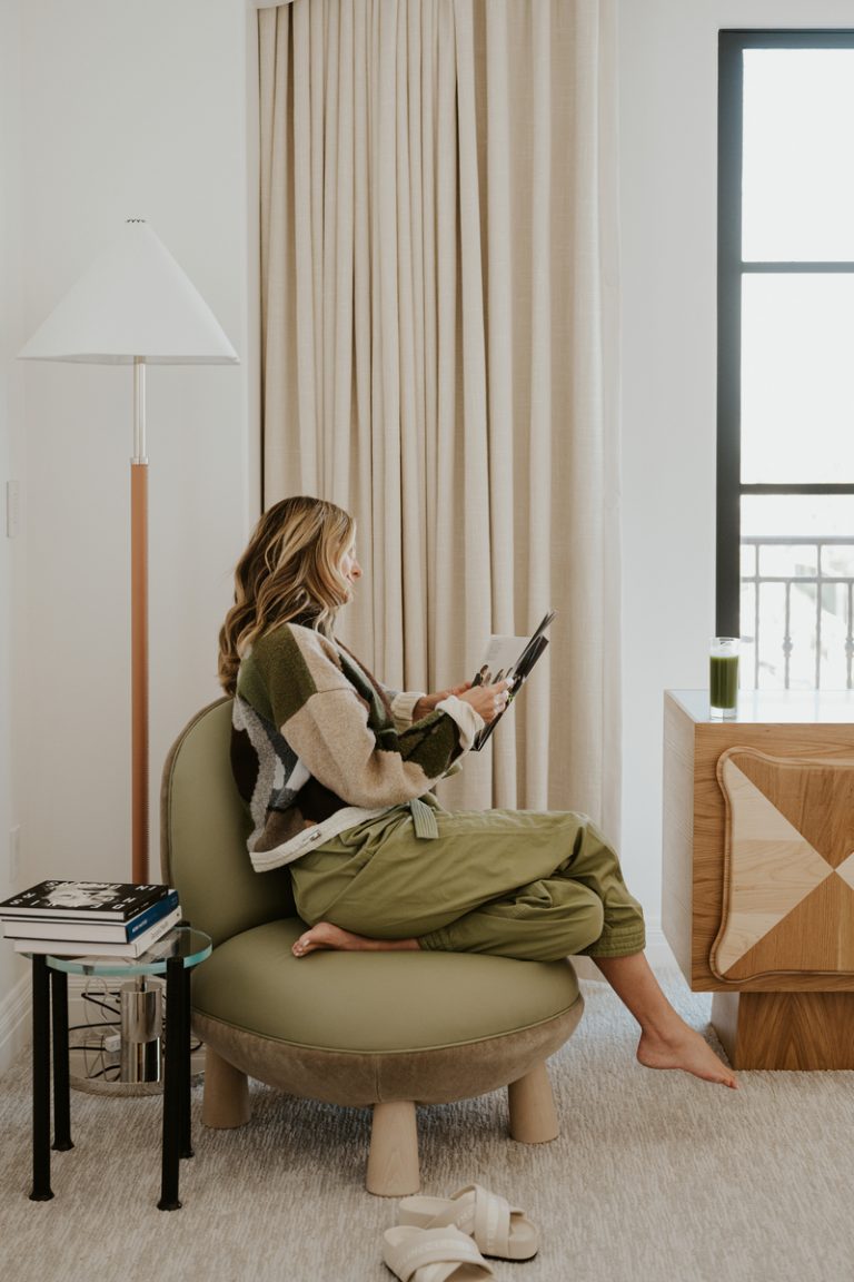 A blonde woman is reading a magazine in an armchair.
