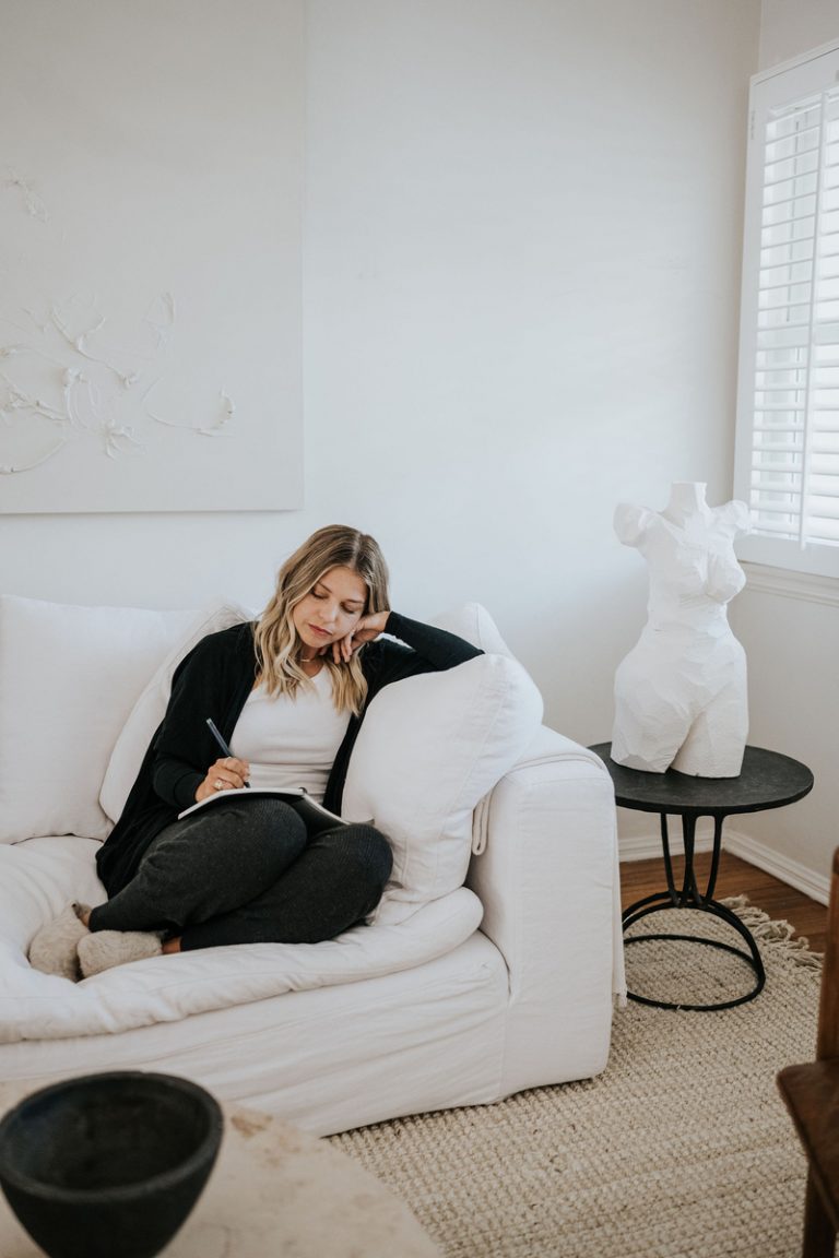 Blonde woman journaling on white couch.