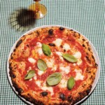 Full Margherita pizza on green checked gingham tablecloth.