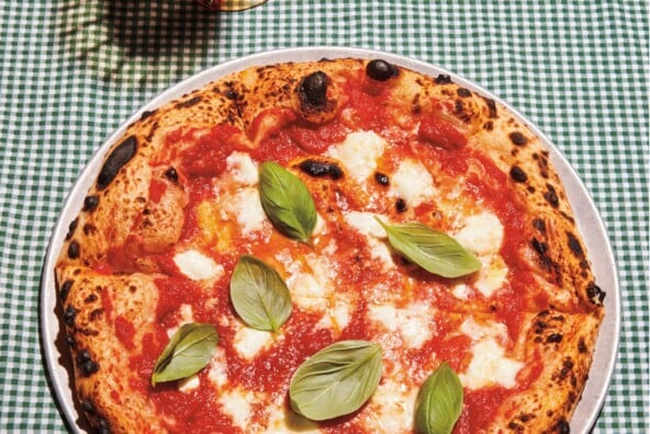 Full Margherita pizza on green checked gingham tablecloth.