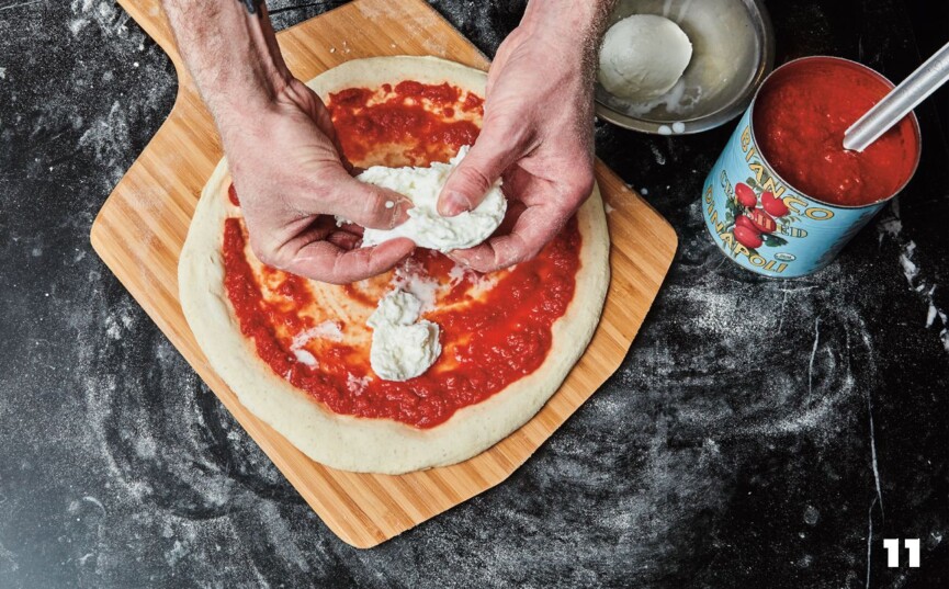 Adding mozzarella to Margherita pizza on wooden pizza peel.