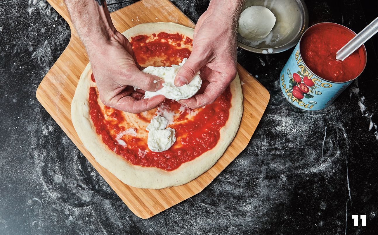 Adding mozzarella to Margherita pizza on wooden pizza peel.