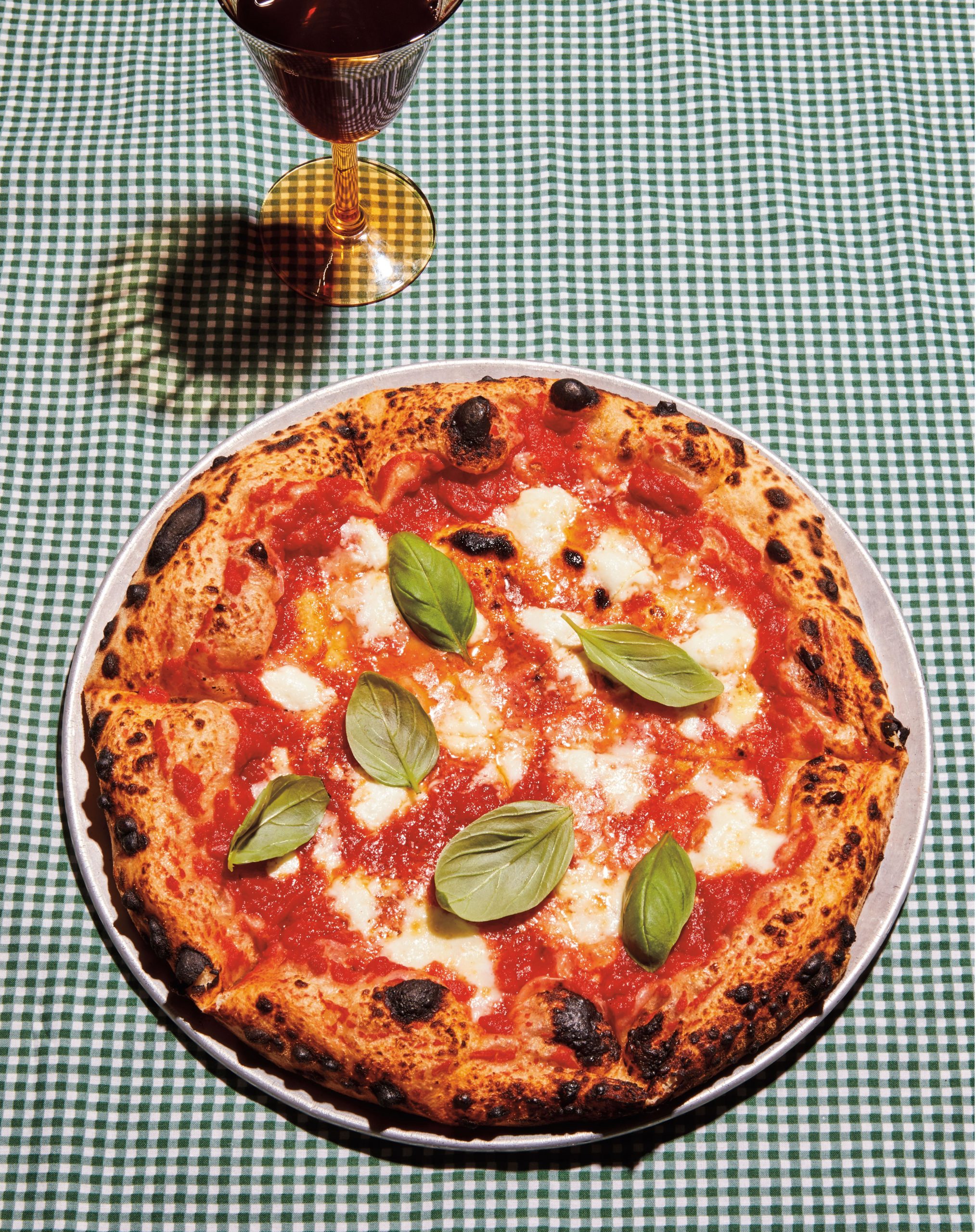 Full Margherita pizza on green checked gingham tablecloth.