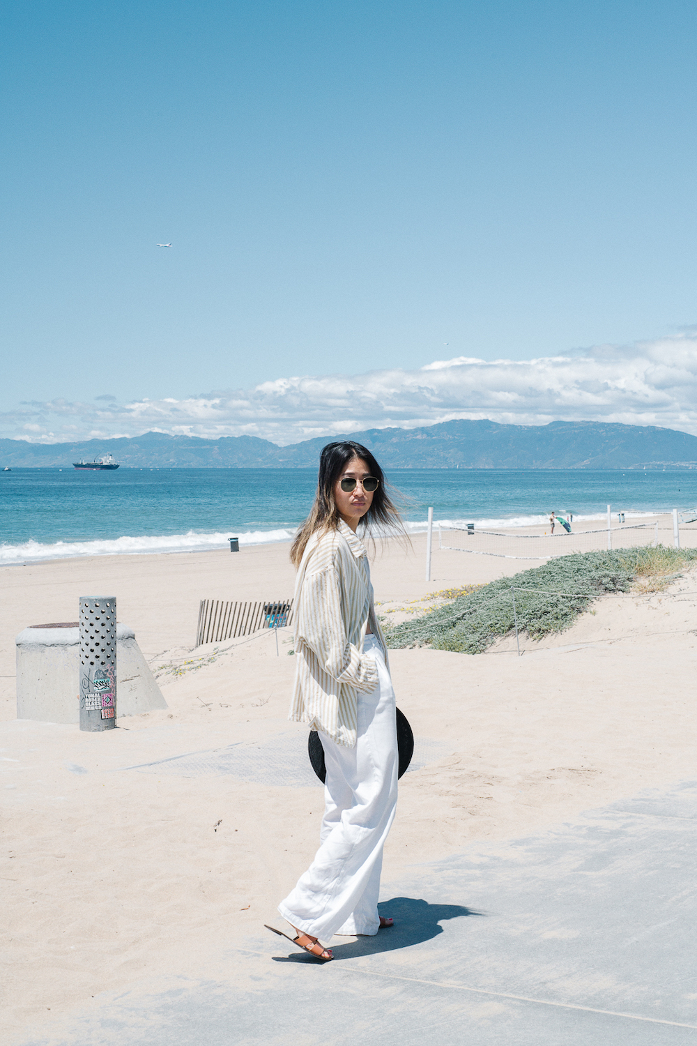 Jenny Yun con una camisa de lino blanca y pantalones en la playa.