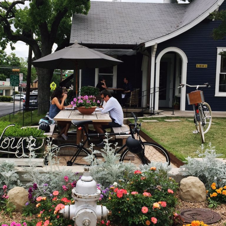 Patio with umbrella-topped picnic tables and garden outside of Josephine House in Austin, Texas.