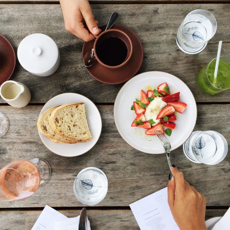 Picnic table with white plates of bread and strawberry mint salad and cups of water, coffee, and rosé wine glasses at Josephine House in Austin.