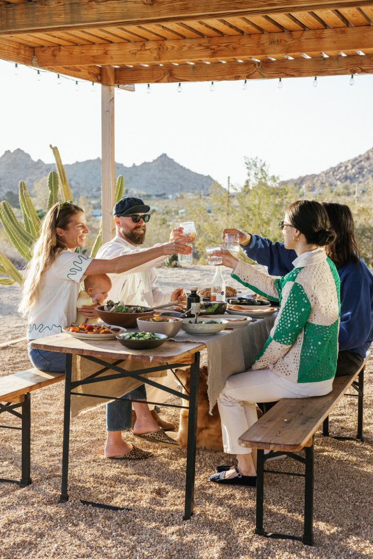 Four people cheers'ing glasses at dinner table in desert. 