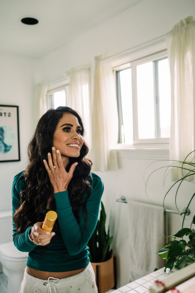 Nutritionist Kimberly Snyder applying skincare in mirror in bathroom.