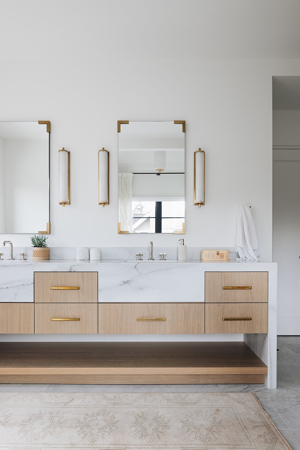 Banheiro moderno branco com pias masculinas e femininas, bancada em mármore e gavetas em madeira clara.